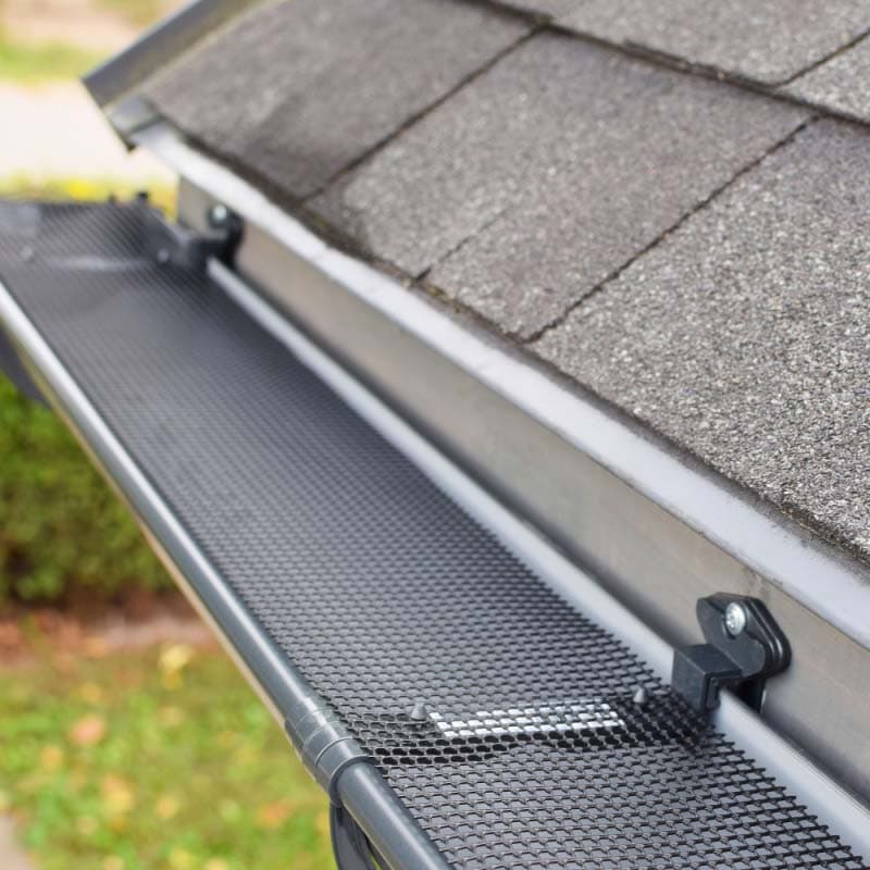 A close-up view of a roof with asphalt shingles and a metal gutter guard installed by a roofing contractor in Suffolk County, NY, designed to prevent leaves and debris from entering and clogging the gutter system.