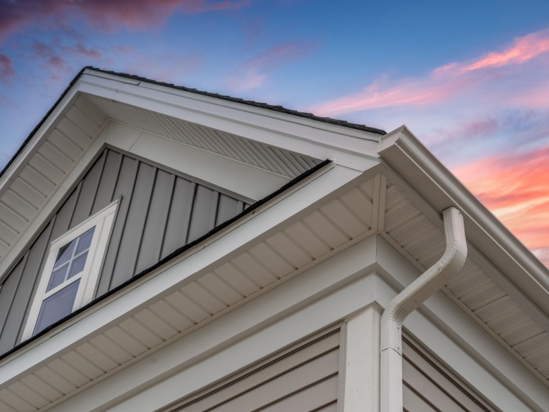 Close-up view of a modern house exterior with white siding, gutter, and window, set against a colorful sunset sky. Perfect inspiration for your next home improvement Suffolk County project.