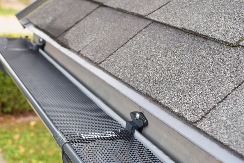 Close-up view of a house roof with gray asphalt shingles and a black mesh gutter guard installed—an essential home improvement Suffolk County residents trust to protect gutters from debris.
