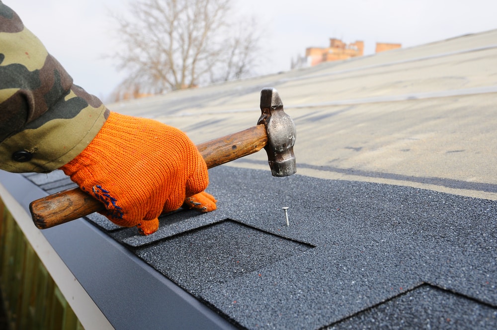 Worker Hands Installing Bitumen Roof Shingles Using Hammer In Nails in Suffolk County, NY