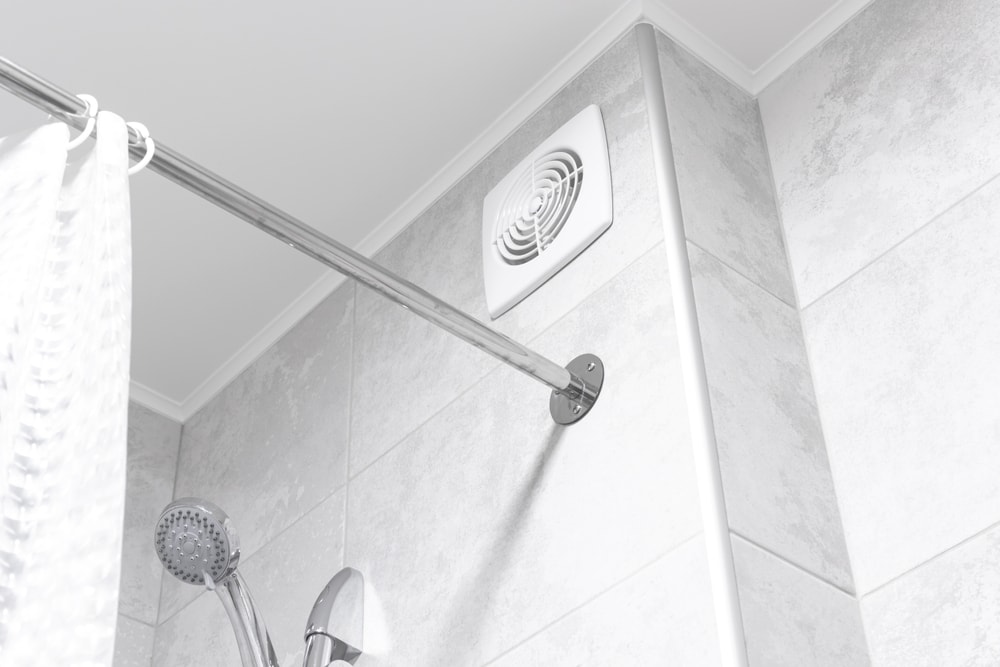 A bathroom with a tiled wall, featuring a mounted showerhead, a metal shower curtain rod with a white curtain, and a ceiling-mounted exhaust fan—a perfect example of home improvement Suffolk County homeowners appreciate.