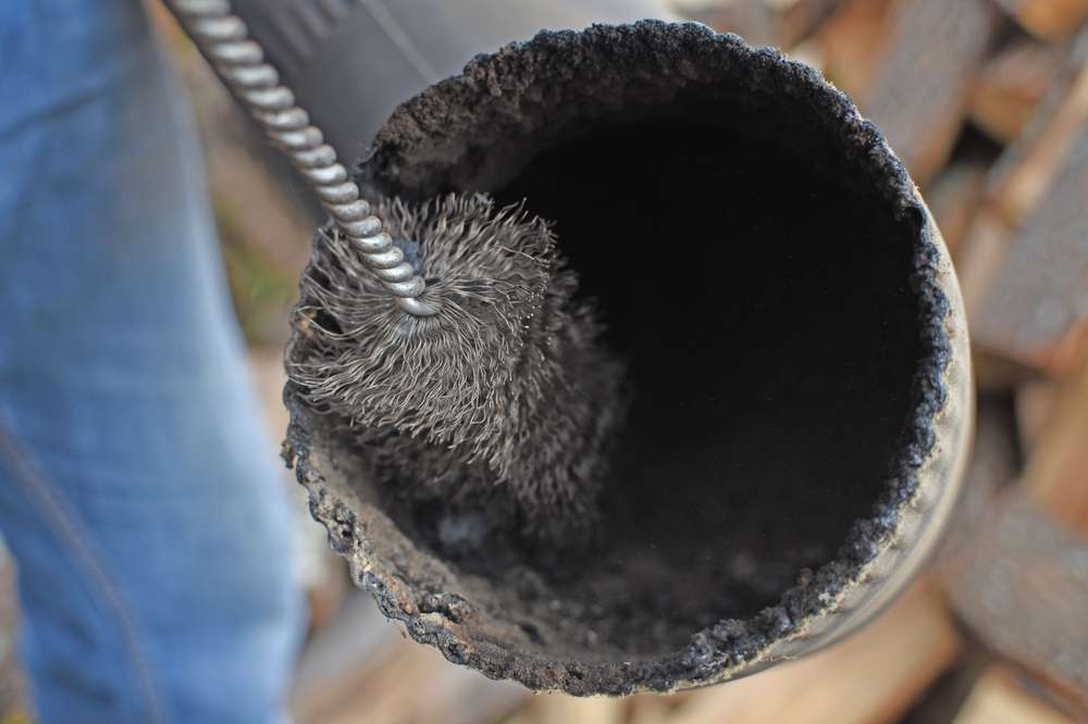 A close-up of a person using a wire brush to clean the inside of a dirty, sooty chimney pipe—a vital home improvement Suffolk County task to tackle heavy soot buildup and maintain safety.