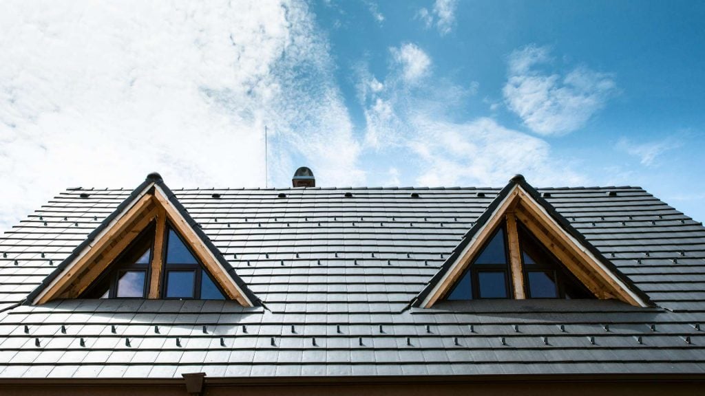 A rooftop with two windows in a triangular shape on roof in Suffolk County, NY with a blue sky